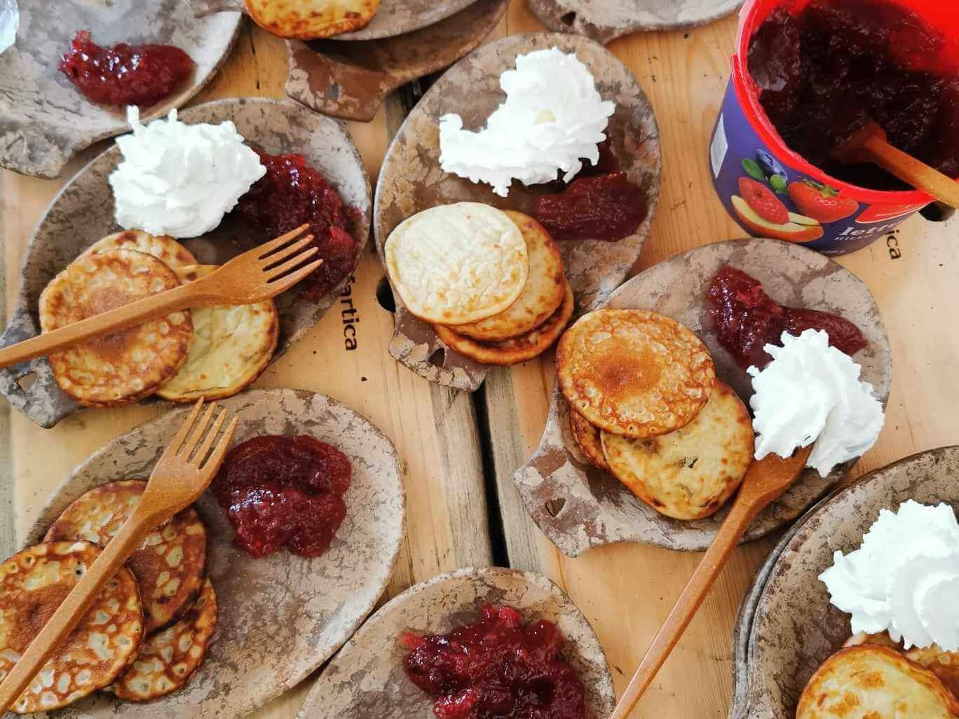 A picnic table with plates of pancakes, jam and cream